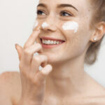 Hautpflege im Frühling: Junge Frau tupft sich Creme auf Wangen und Nase.