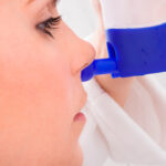 Nasendusche: Eine junge Frau hält eine blau-weiße Nasendusche an die Nase.